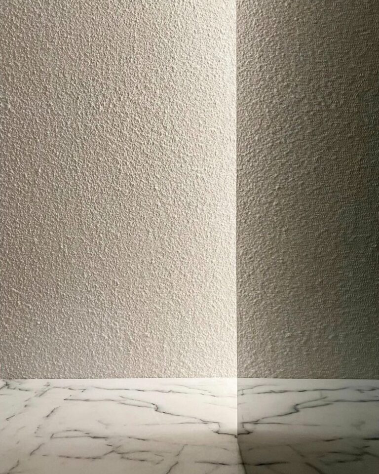 Close-up of a bathroom wall and floor with a textured, mottled gray microcement finish.